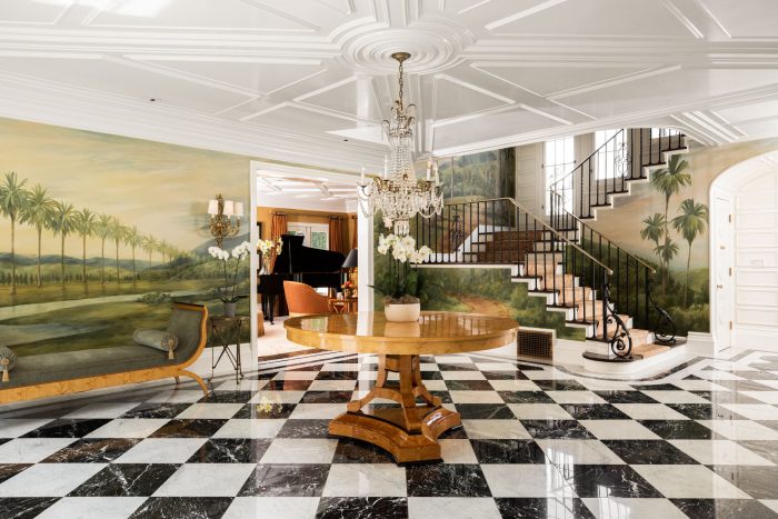 Foyer with paintings of palm trees and checkered marble floor.