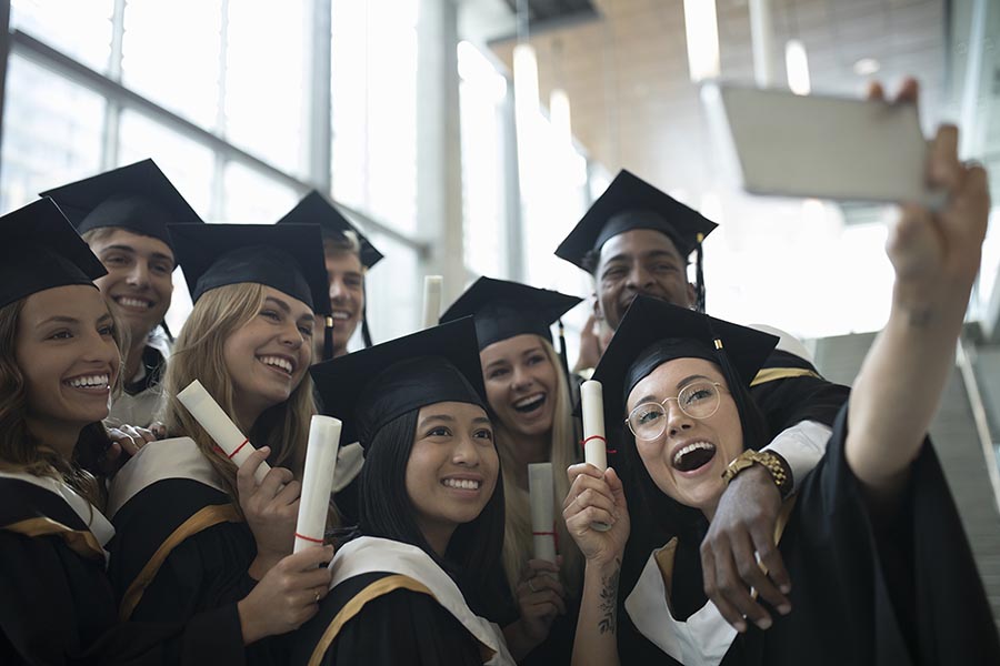College student graduate friends in caps and gowns taking selfie with camera phone