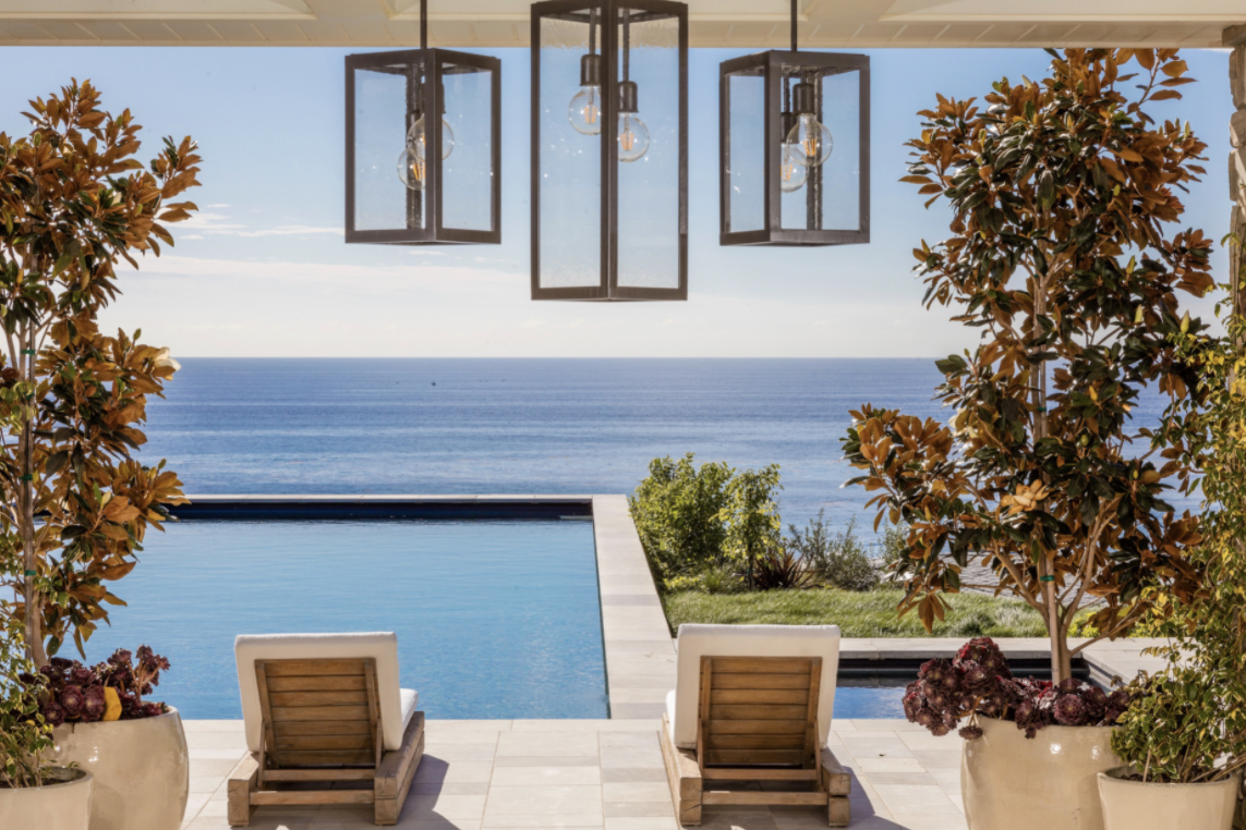 Pool chairs pool ocean and light fixtures over deck in the day time