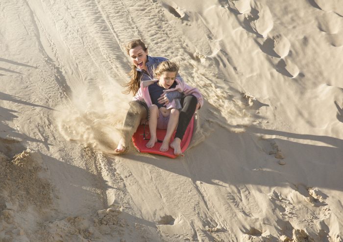 Two kids sledding on the sand.